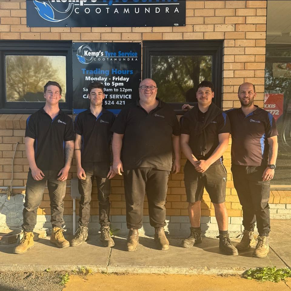 The Kemp's Tyre Service team standing outside the workshop beside the trading hours sign