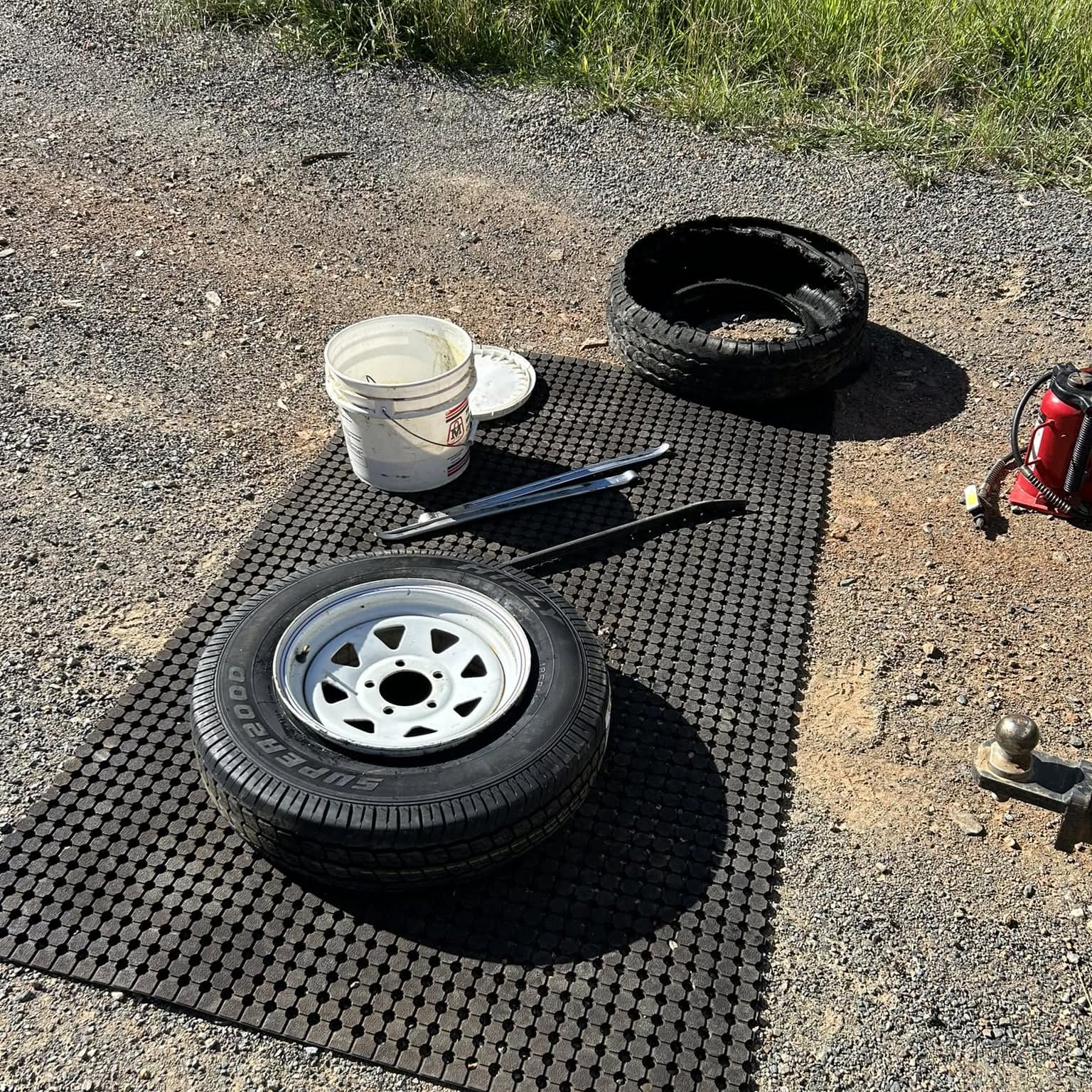 A trailer wheel and tyre levers laid out on a mat on gravel during an on-site tyre change